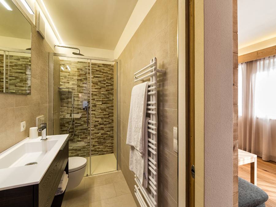 Weißes Waschbecken mit dunklem Holzschrank darunter und Regendusche im Hintergrund - Kiebacher Wahlen