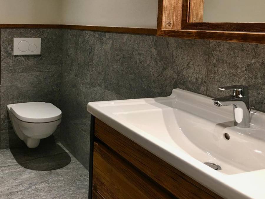 Weißes Waschbecken mit Holzschrank darunter, im Hintergrund ein WC - Kiebacher Wahlen